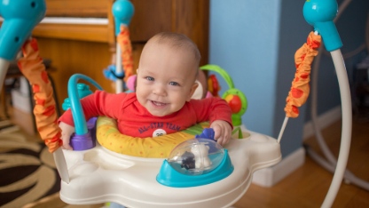 One year toddler boy jumping in a jumper at home.