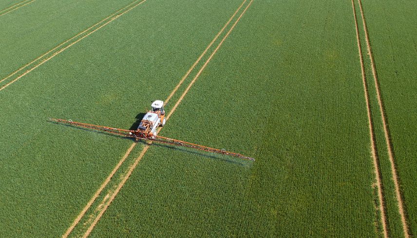Aerial view of a tractor applying spray to a large agricultural field, showcasing farming practices from above.