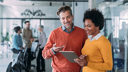 Man and woman smiling while looking at electronic tablet in office setting
